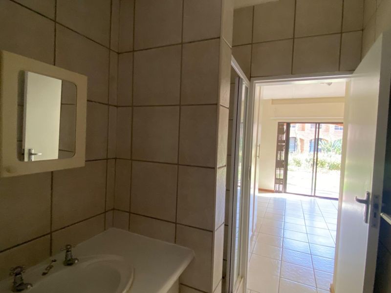 A functional bathroom featuring tiled walls and flooring, a vanity basin, and a wall-mounted mirror cabinet, with direct access to the living area.