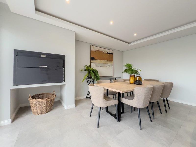 Modern dining area featuring a built-in indoor braai, recessed ceiling lighting, and neutral large-format floor tiles.