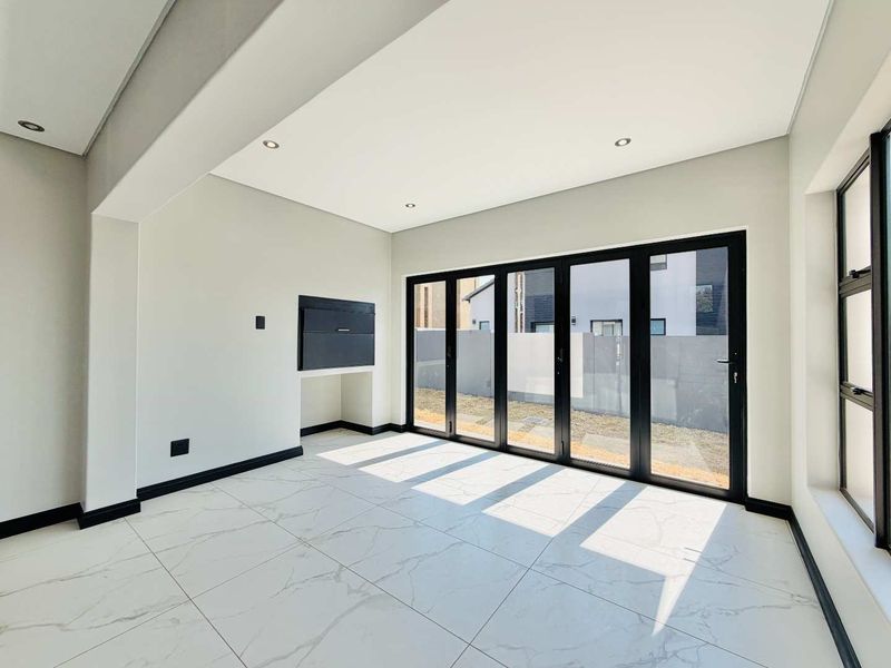 Bright and modern living area featuring large format marble-look floor tiles, recessed lighting, and black aluminium stacker doors opening to the garden.