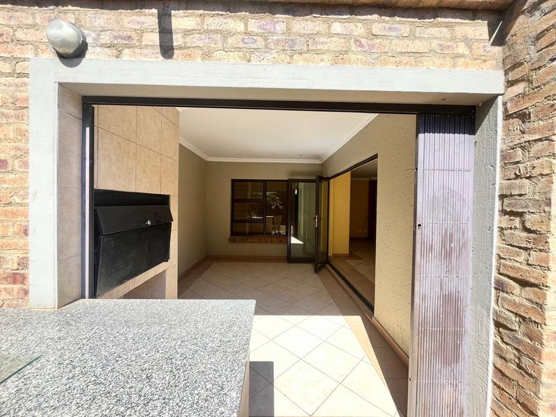 Covered patio area featuring a built-in braai, granite prep counter, and tiled flooring, providing a seamless transition to the interior living space.
