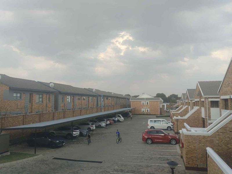 An elevated view of a residential apartment complex featuring brick facades, tiled roofs, and covered carport parking bays within a paved courtyard.