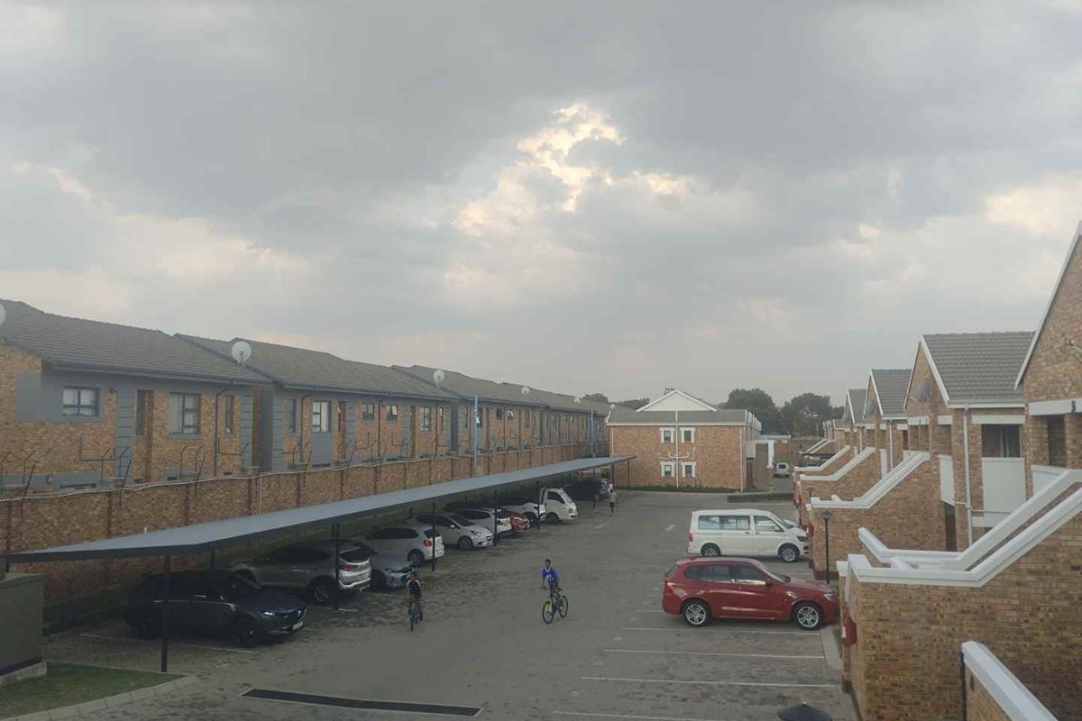 An elevated view of a residential apartment complex featuring brick facades, tiled roofs, and covered carport parking bays within a paved courtyard.