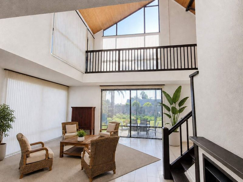 Spacious double-volume living area featuring a vaulted timber ceiling, mezzanine balcony, and large windows providing abundant natural light and garden access.
