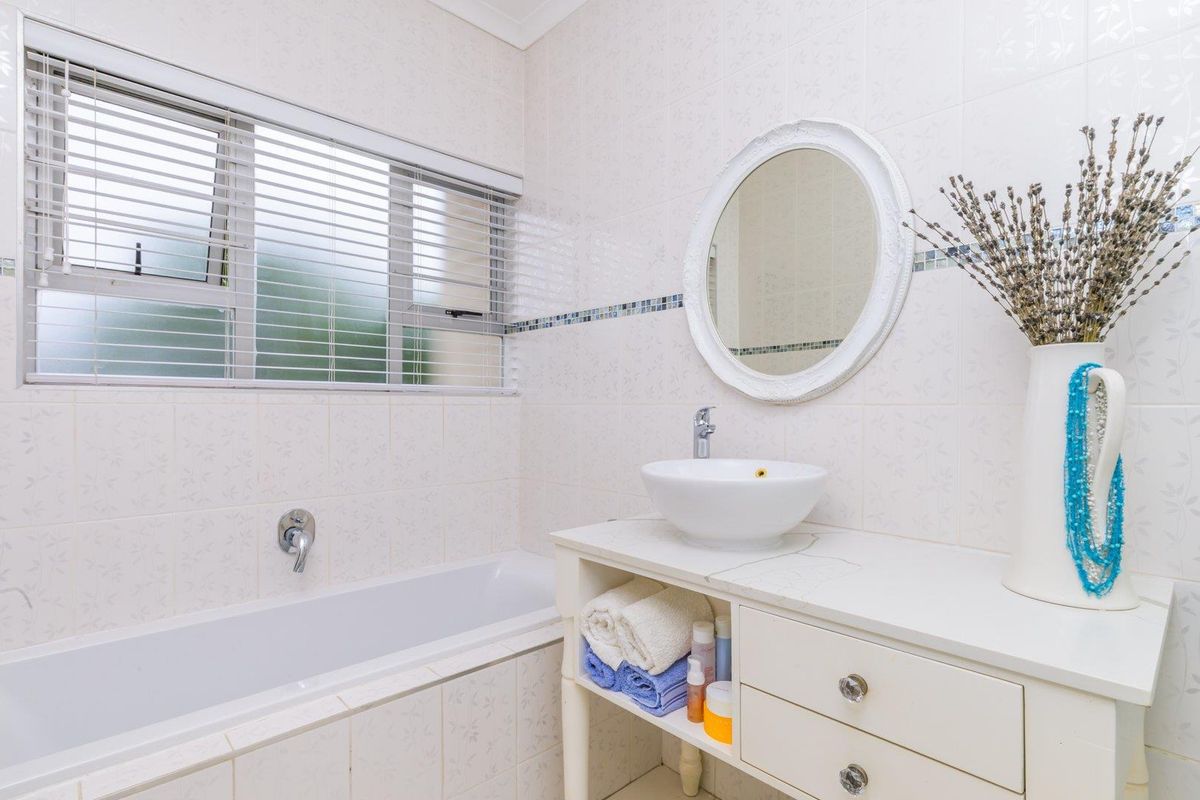 A functional bathroom featuring a built-in bathtub, a vessel sink vanity with storage drawers, and a window with fitted blinds.