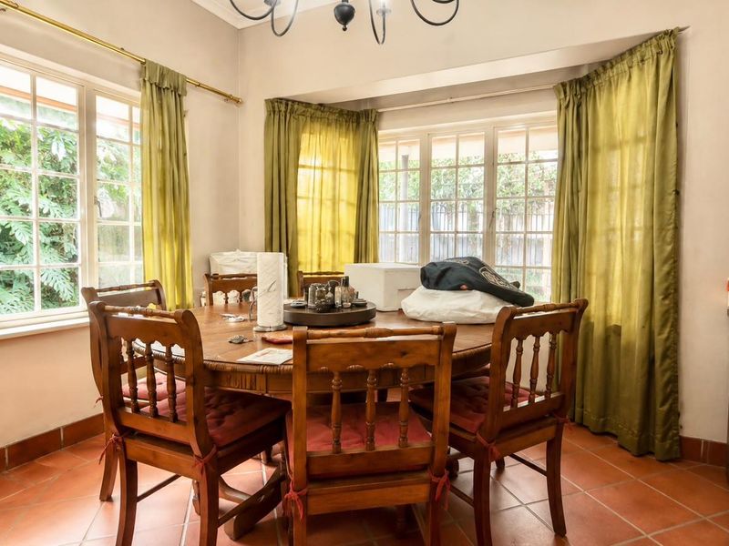 A dining area featuring terracotta floor tiles and large multi-pane windows that provide ample natural light and garden views.