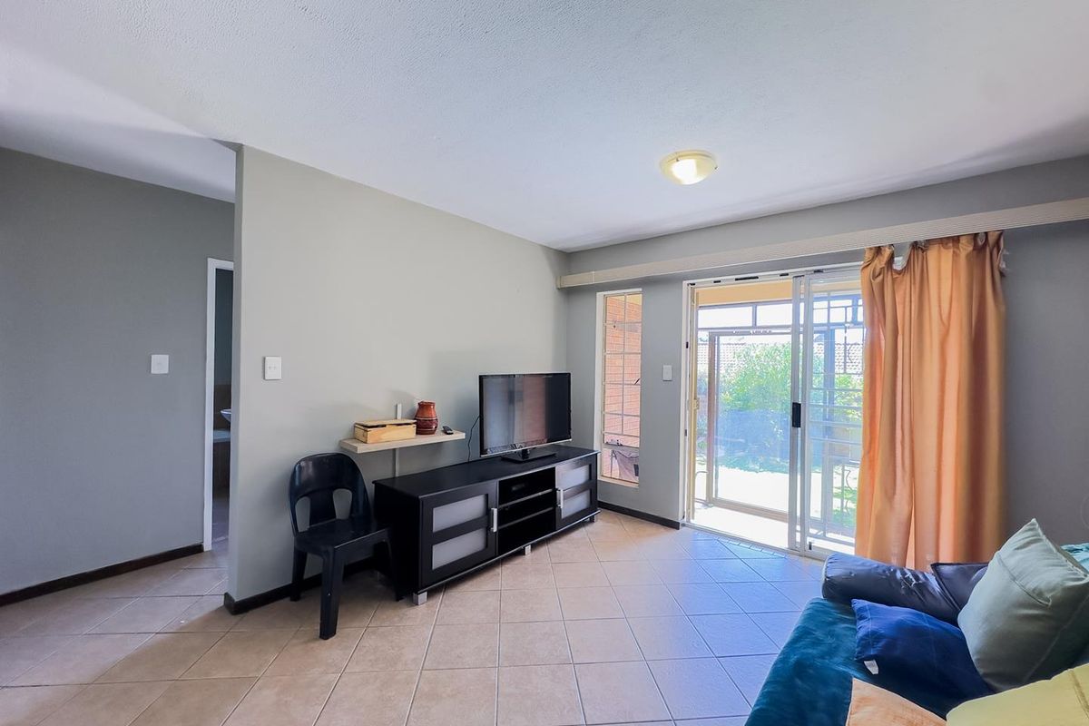 A living room featuring tiled flooring and a sliding glass door with security gate, providing direct access to the outdoor area.