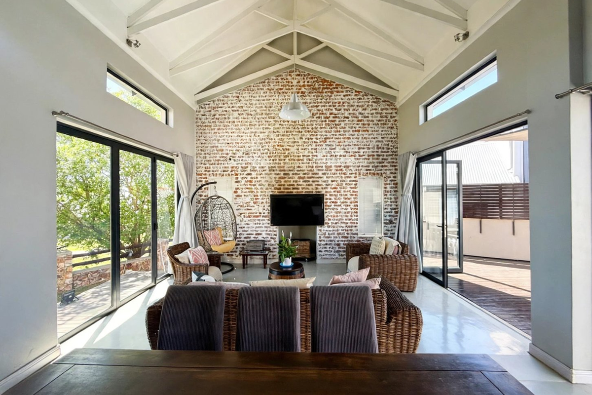 Spacious living room featuring a striking exposed brick wall, vaulted ceilings with exposed trusses, and large sliding doors opening to outdoor areas.