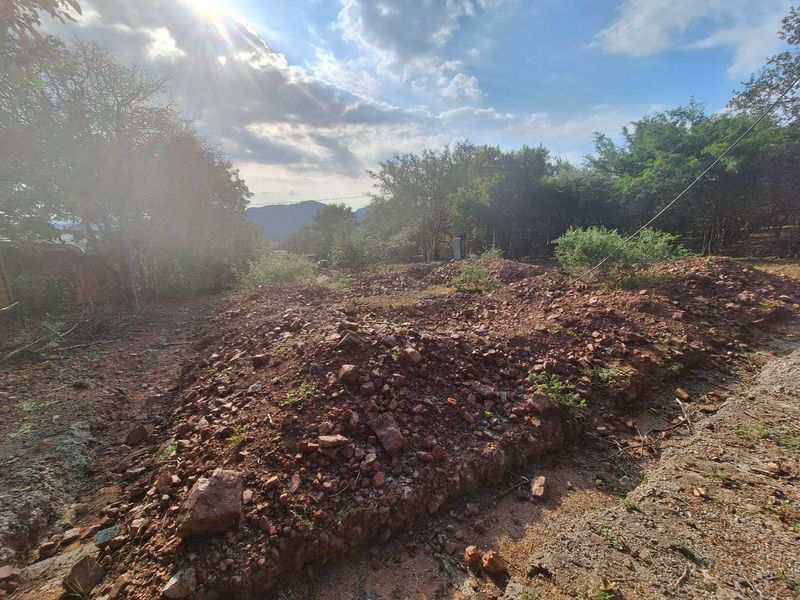 A view of an undeveloped residential plot featuring natural vegetation and rocky, uneven terrain.