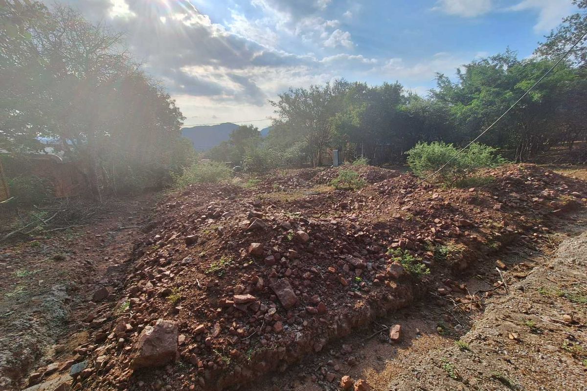 A view of an undeveloped residential plot featuring natural vegetation and rocky, uneven terrain.