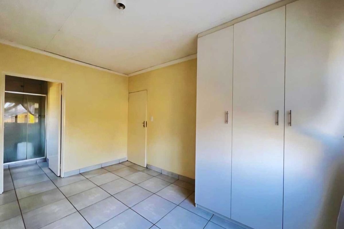 A bedroom featuring built-in wardrobes, tiled flooring, and an adjoining bathroom entrance.
