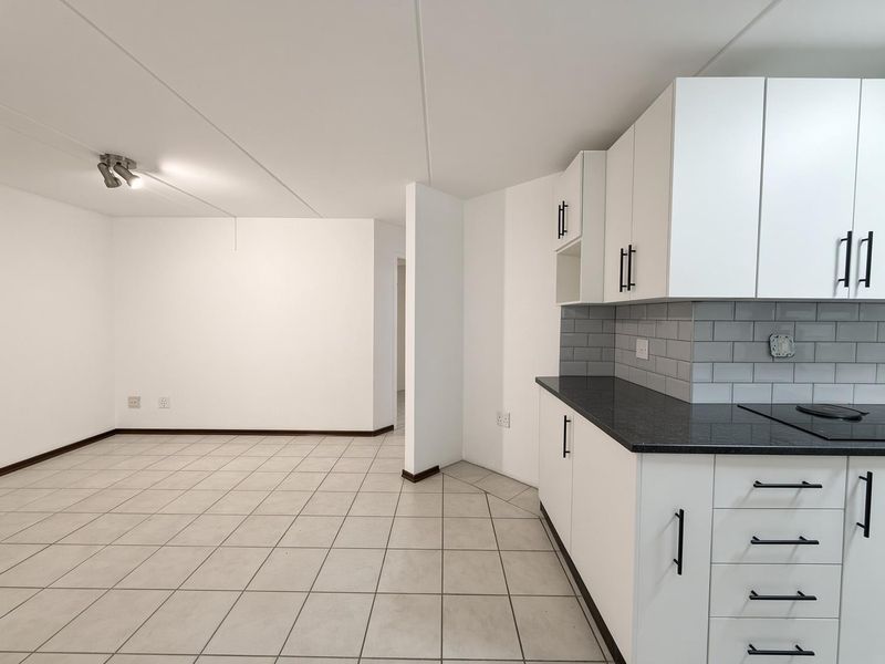 A bright, open-plan living and kitchen area featuring modern white cabinetry, dark granite countertops, and neutral ceramic floor tiles.
