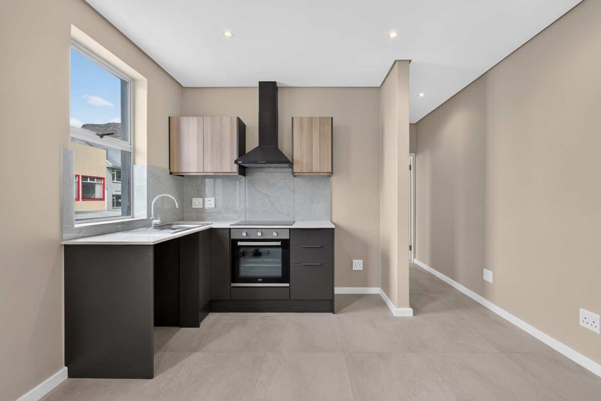 Modern kitchen featuring dark cabinetry, integrated oven and hob, extractor fan, and stone-look splashback, finished with neutral floor tiles and recessed lighting.