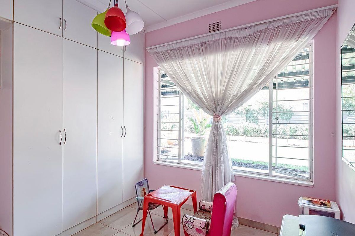A bedroom featuring built-in floor-to-ceiling wardrobes, tiled flooring, and large windows with security bars overlooking the exterior.