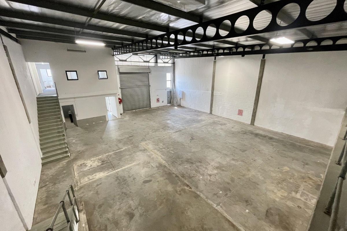 Spacious industrial warehouse unit featuring high ceilings with exposed steel trusses, concrete flooring, and a large roller shutter door for easy access.