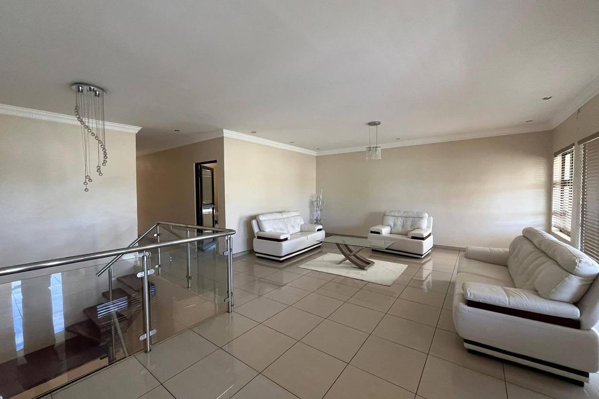 Spacious open-plan living area featuring polished floor tiles, recessed downlighting, and a modern glass and stainless steel staircase balustrade.