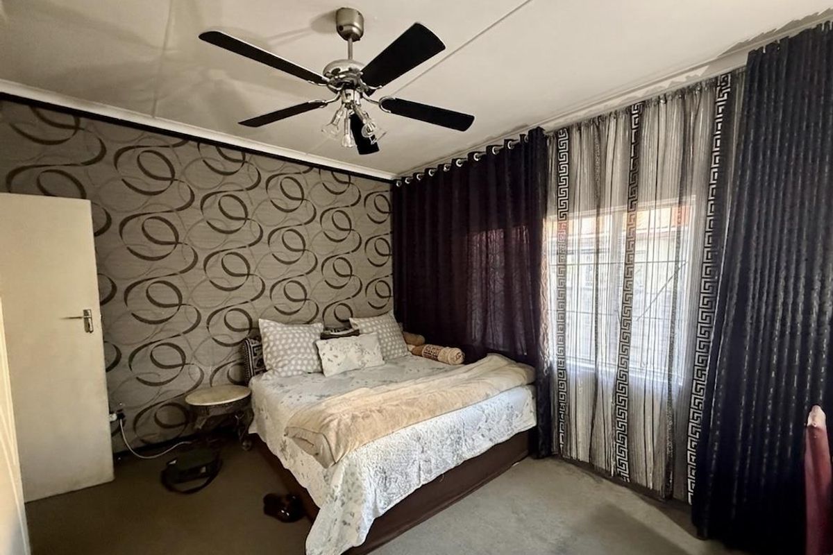 A bedroom featuring a ceiling fan, patterned accent wall, and large window with curtain treatments.