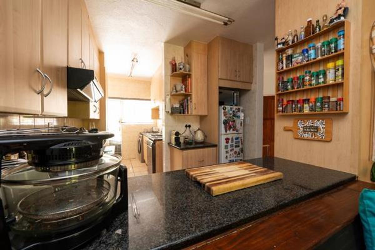 A functional kitchen featuring granite countertops, light wood cabinetry, and an integrated layout with a breakfast bar and adjacent scullery area.