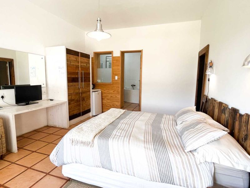 A bedroom featuring terracotta floor tiles, built-in wooden wardrobe, integrated desk space, and direct access to an en-suite bathroom.