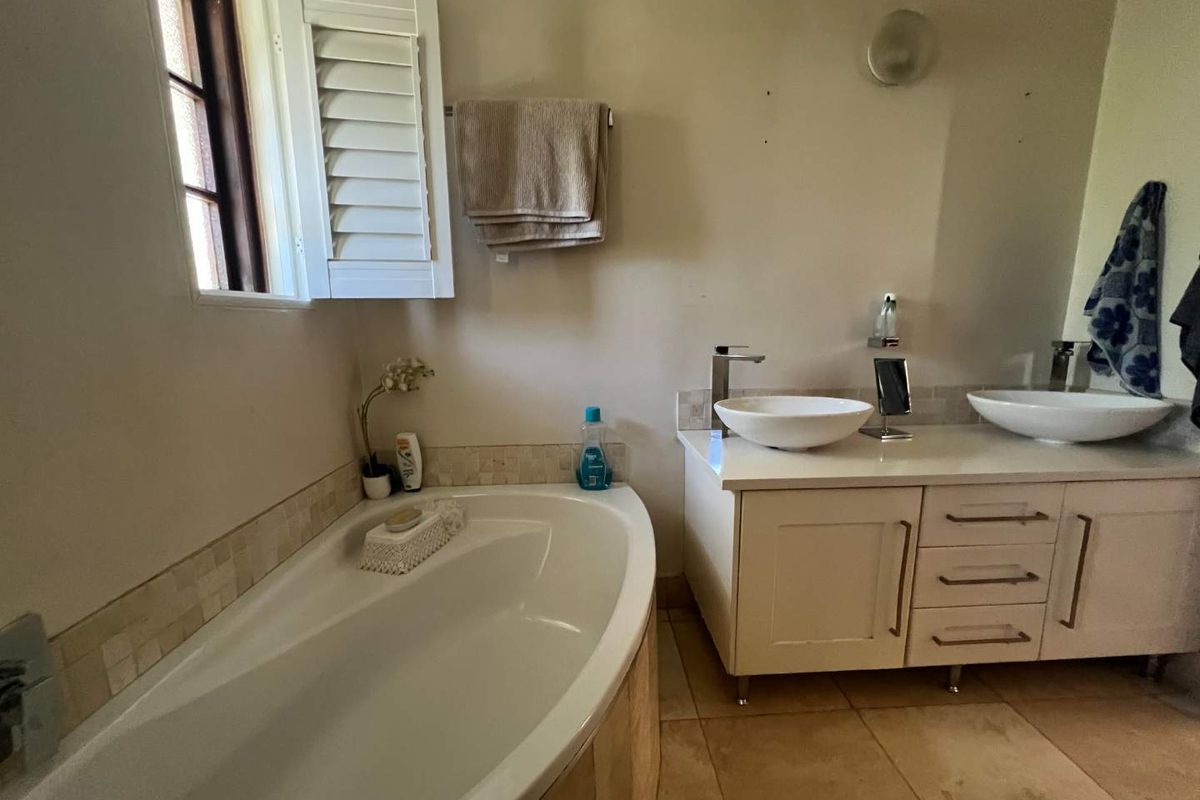 A well-appointed bathroom featuring a built-in bathtub, dual vessel sinks on a vanity unit, and tiled finishes with shutter window detailing.