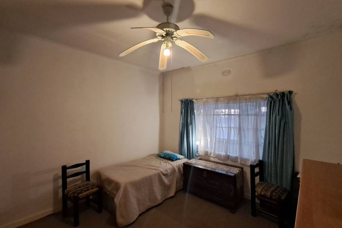 A bedroom featuring a ceiling fan and a window with curtain tracks, requiring cosmetic updates to the walls and ceiling.