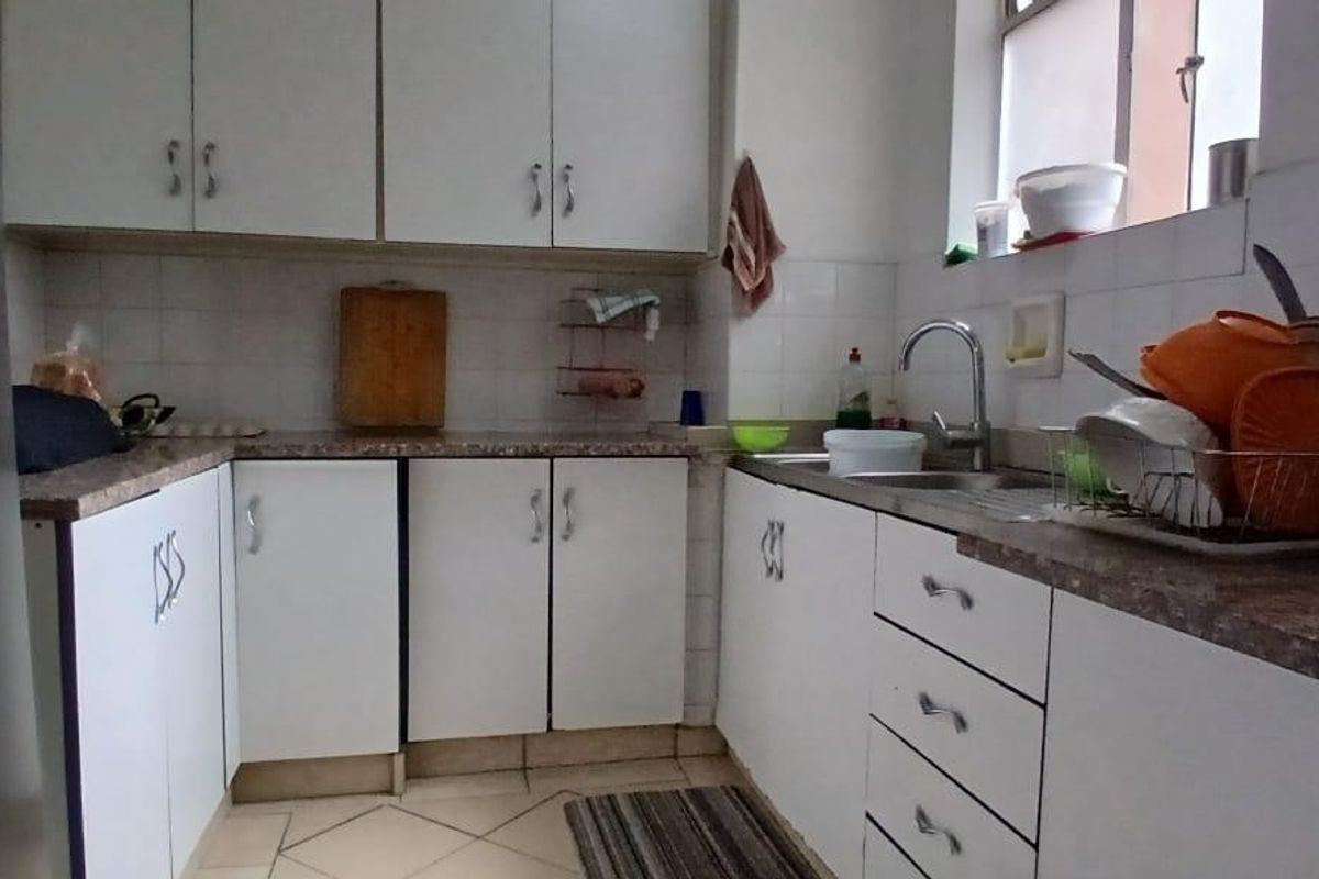 A functional kitchen featuring white cabinetry, laminate countertops, a stainless steel sink, and tiled finishes, offering a practical layout for daily meal preparation.