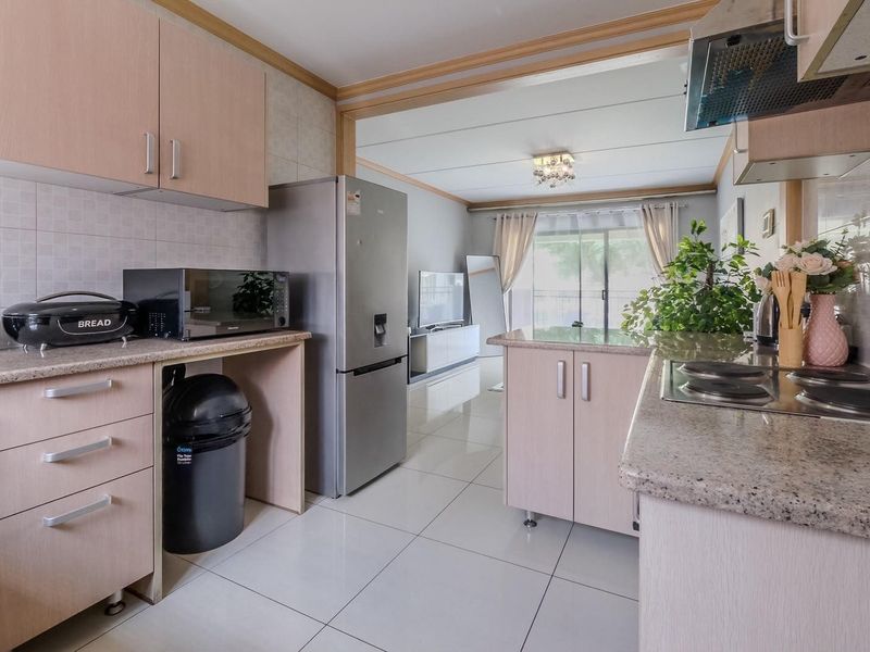 Open-plan kitchen and living area featuring light wood cabinetry, granite countertops, electric hob, extractor fan, and tiled flooring leading to a balcony.