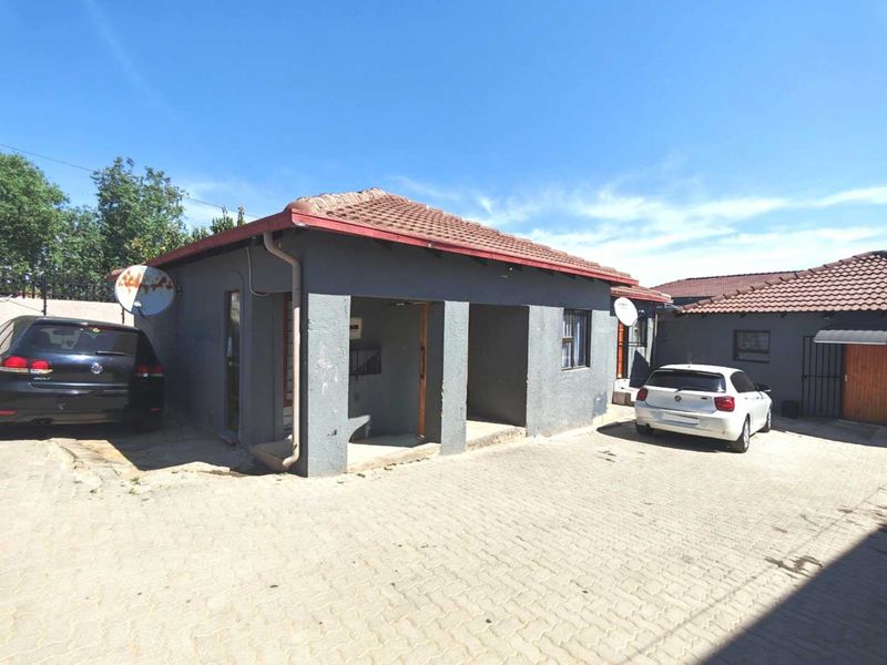 Front exterior view of a single-story house featuring a tiled roof, textured grey walls, and a paved driveway area.