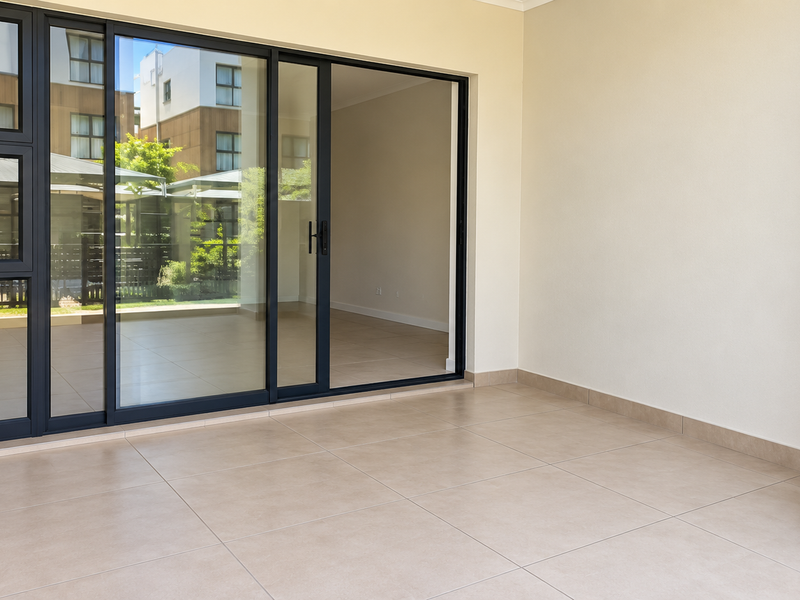 A clean, empty covered patio featuring large sliding glass doors and neutral floor tiles, offering a seamless transition to the interior living space.