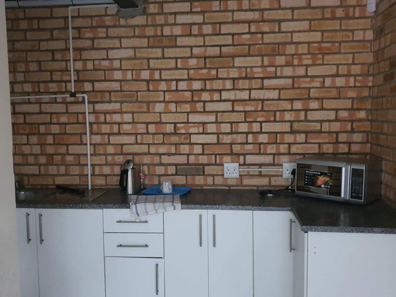 A functional kitchenette featuring exposed brick walls, white base cabinetry, a laminate countertop, and a stainless steel sink.