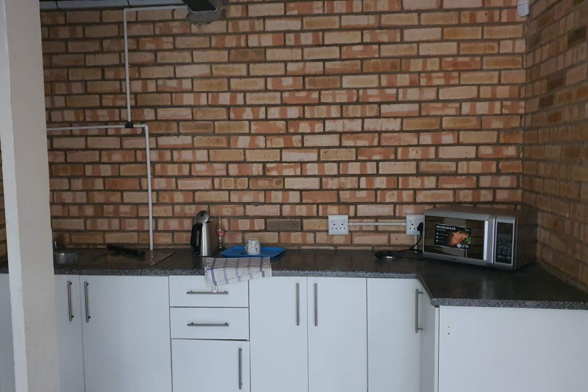 A functional kitchenette featuring exposed brick walls, white base cabinetry, a laminate countertop, and a stainless steel sink.
