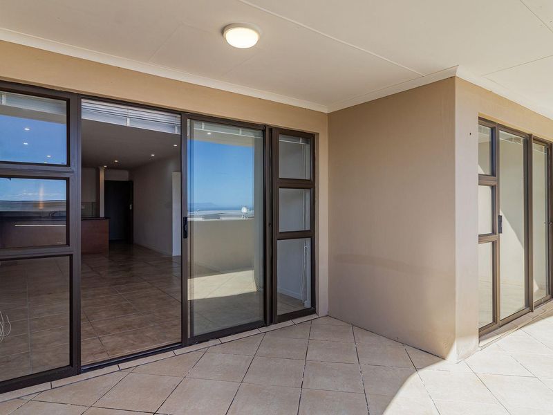 A spacious covered balcony featuring tiled flooring and large sliding glass doors providing seamless access to the interior living area.