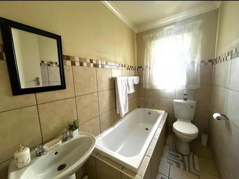 A functional bathroom featuring a pedestal basin, built-in bathtub, and toilet with neutral wall and floor tiling.