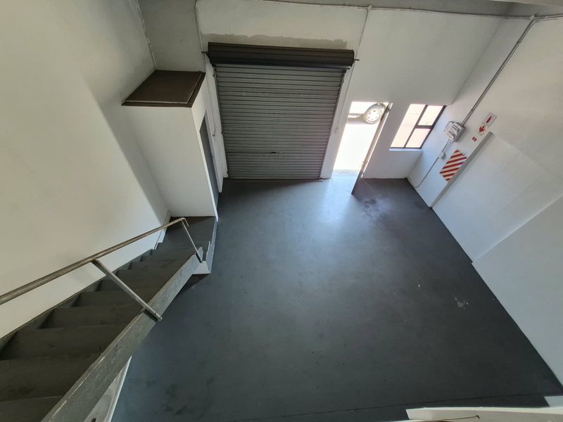Industrial utility space featuring a roller shutter door, metal staircase, and durable epoxy flooring, suitable for storage or workshop use.