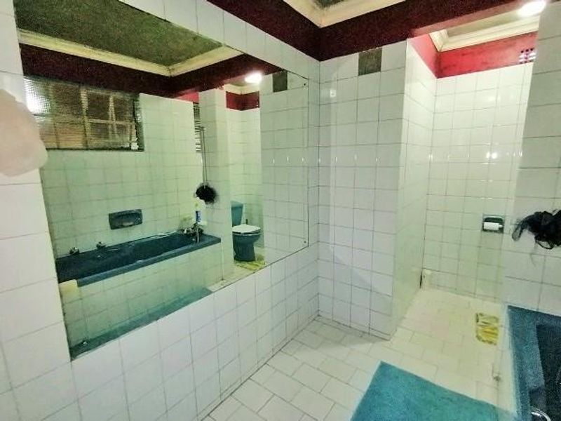 A dated bathroom featuring a built-in bathtub, toilet, and large wall mirror with white ceramic tiling throughout.