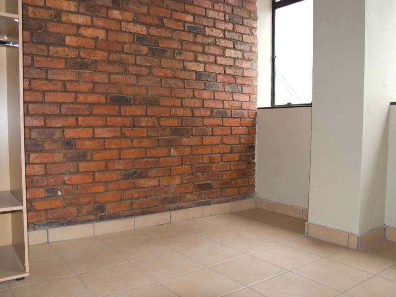 A bedroom featuring an exposed brick feature wall, neutral tiled flooring, and a built-in cupboard.