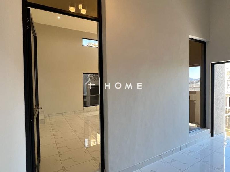 A bright, modern hallway featuring high ceilings, polished porcelain floor tiles, and sleek black aluminium door frames leading to adjacent living spaces.