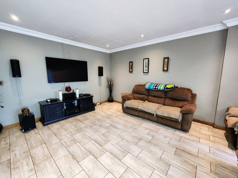 A comfortable living room featuring neutral wall tones, crown molding, recessed lighting, and durable ceramic tile flooring throughout the space.