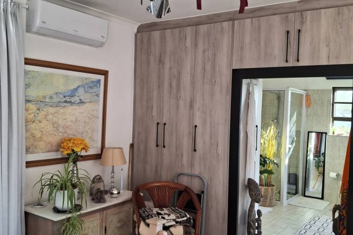 A well-maintained bedroom featuring built-in cupboards, an air conditioning unit, and direct access to an en-suite bathroom with a shower.