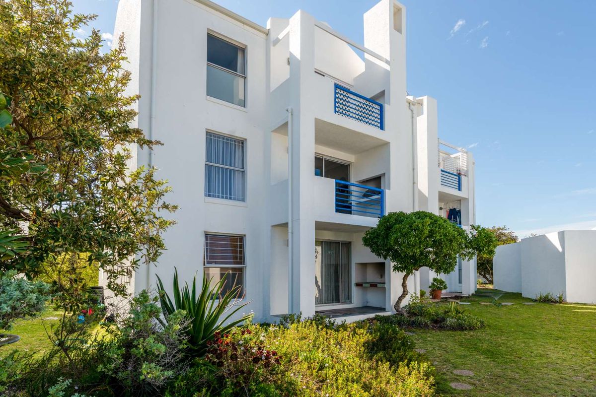 Rear view of a multi-story apartment building featuring private balconies, sliding glass doors, and a built-in braai area overlooking a landscaped garden.
