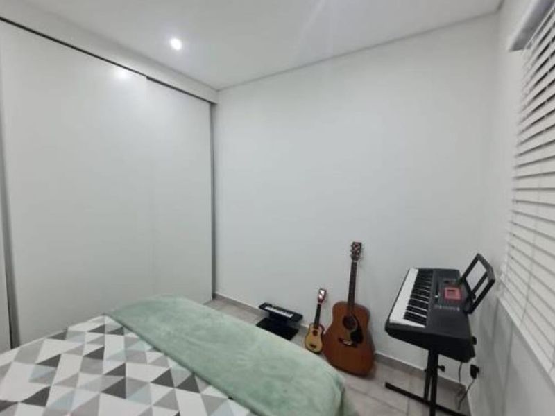 A clean bedroom featuring a large built-in sliding door wardrobe, neutral walls, and venetian blinds for adjustable natural light.