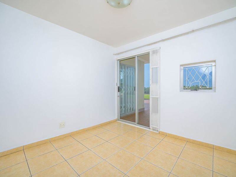 An empty, neutrally painted living area featuring ceramic floor tiles, a sliding glass door leading to the patio, and security window bars.
