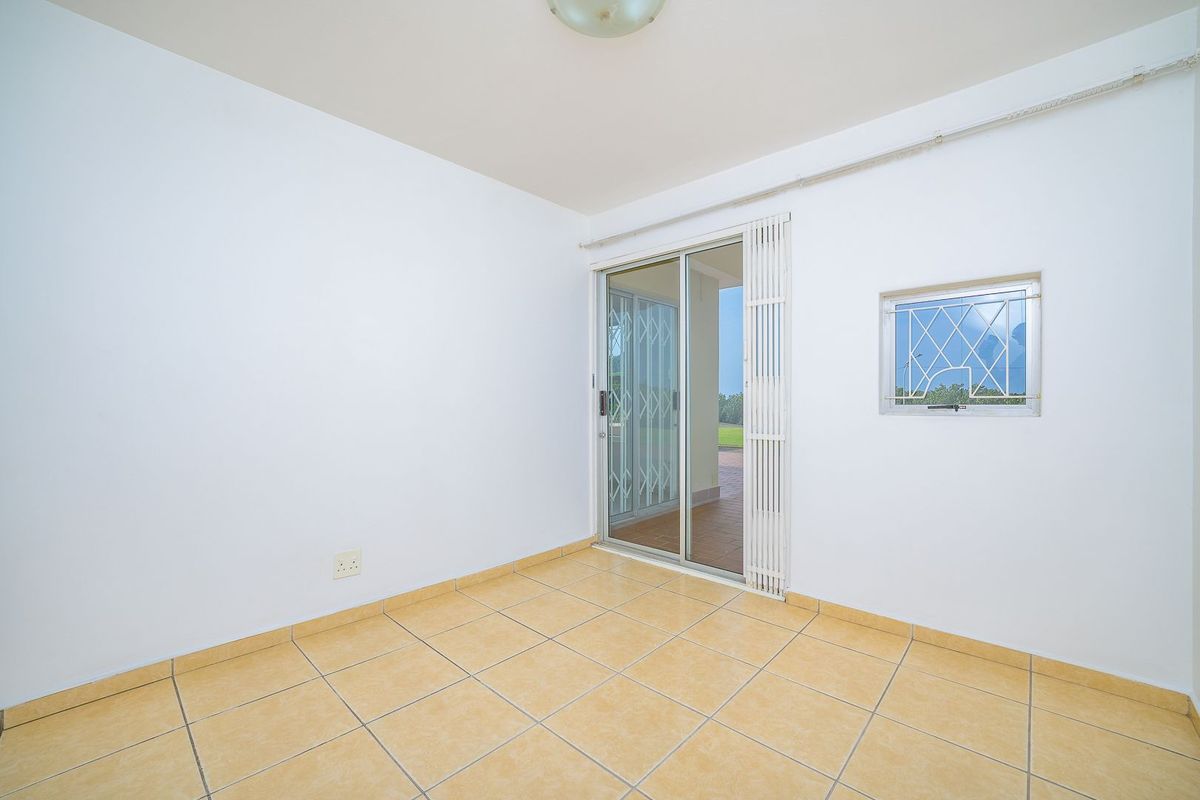 An empty, neutrally painted living area featuring ceramic floor tiles, a sliding glass door leading to the patio, and security window bars.