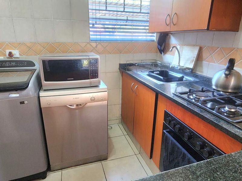 Compact kitchen featuring granite countertops, gas hob, built-in oven, and tiled backsplash with functional cabinetry and space for laundry appliances.