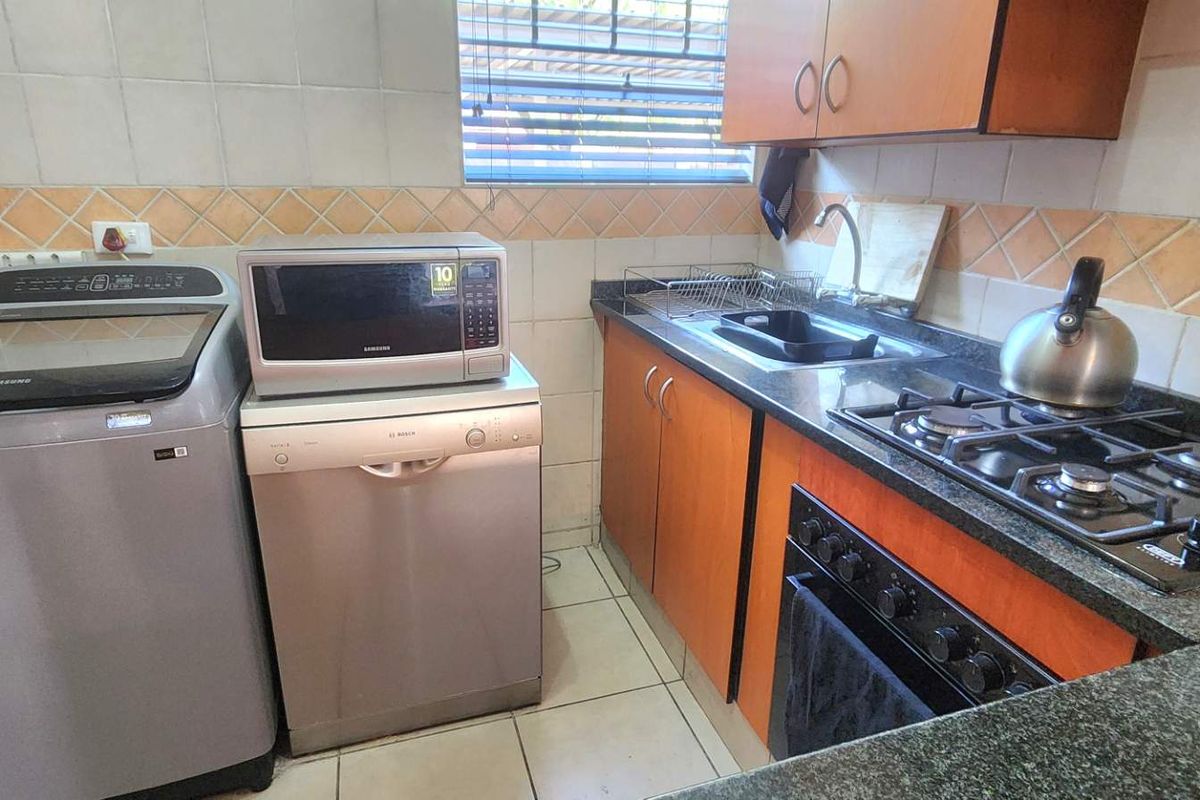 Compact kitchen featuring granite countertops, gas hob, built-in oven, and tiled backsplash with functional cabinetry and space for laundry appliances.