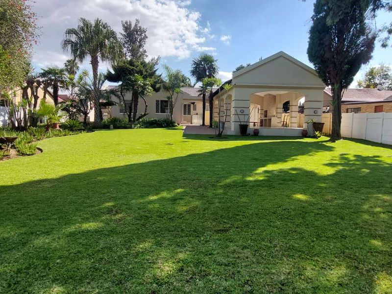 Spacious rear garden featuring a well-maintained lawn, mature trees, and a covered patio area with a built-in braai, perfect for outdoor entertaining.