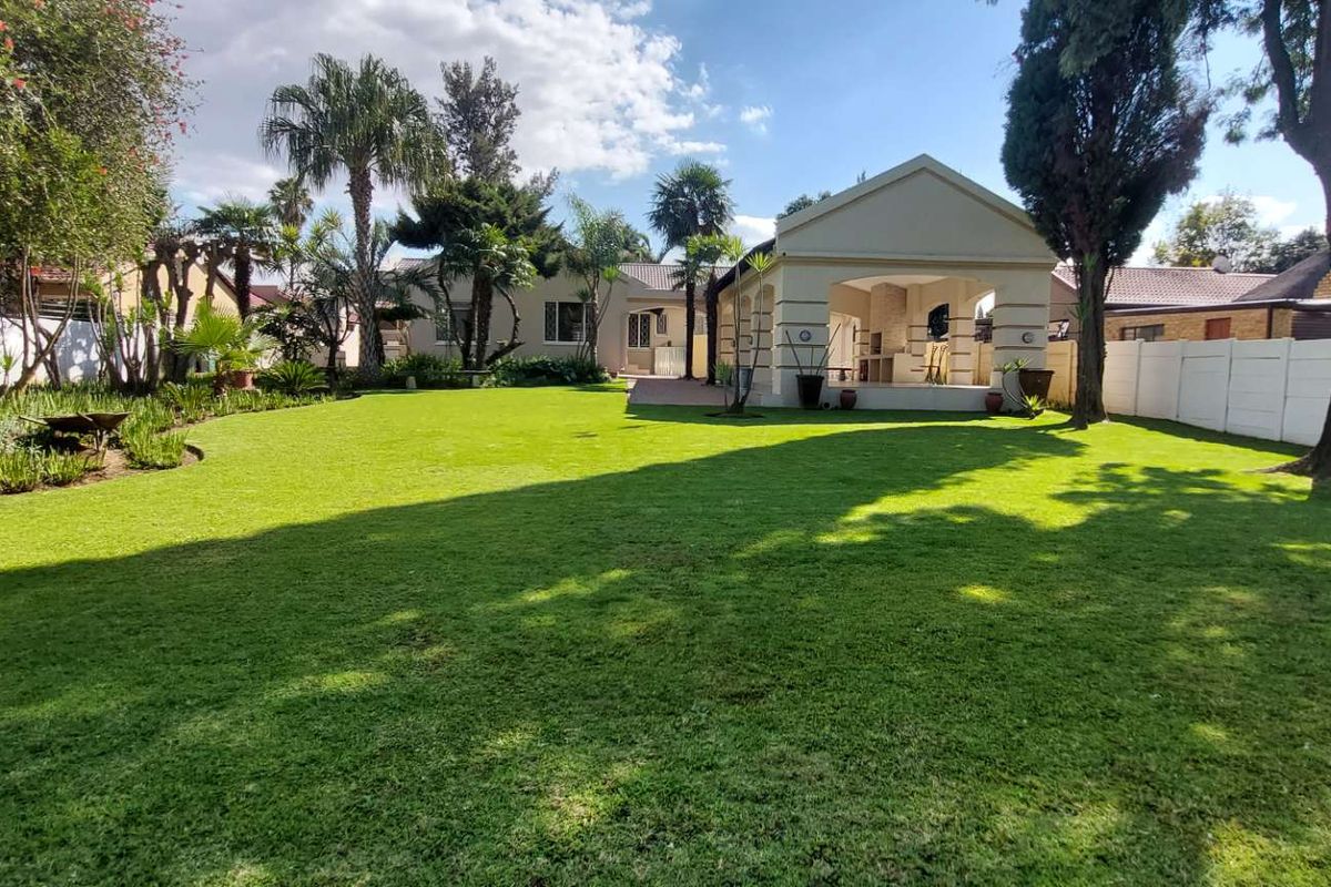 Spacious rear garden featuring a well-maintained lawn, mature trees, and a covered patio area with a built-in braai, perfect for outdoor entertaining.