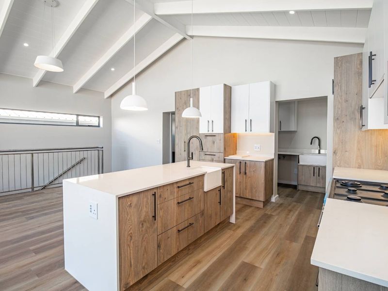 Modern open-plan kitchen featuring a central island, quartz countertops, farmhouse sink, gas hob, and vaulted ceilings with exposed beams, adjacent to a functional scullery.