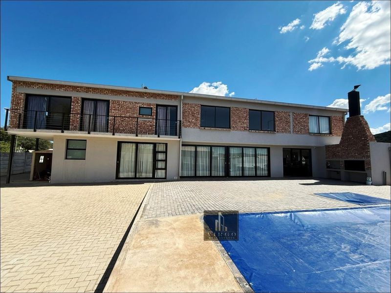 Rear view of a two-story house featuring a brick facade, balcony, paved patio area, and a swimming pool with a built-in outdoor braai.