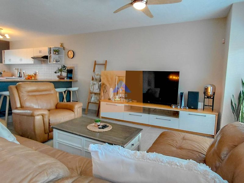 Spacious open-plan living area featuring a modern kitchen with breakfast bar, integrated cabinetry, and a ceiling fan, flowing into a comfortable lounge space.