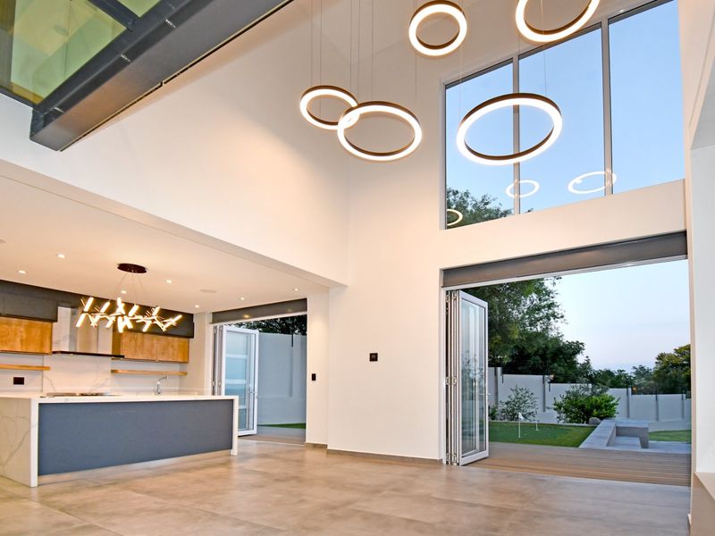 Spacious open-plan living area featuring a modern kitchen with stone island, double-volume ceilings, and seamless indoor-outdoor flow through large bi-fold doors.